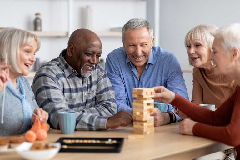 An older adult sits in a warmly lit communal living area beside a caregiver reviewing paperwork together.